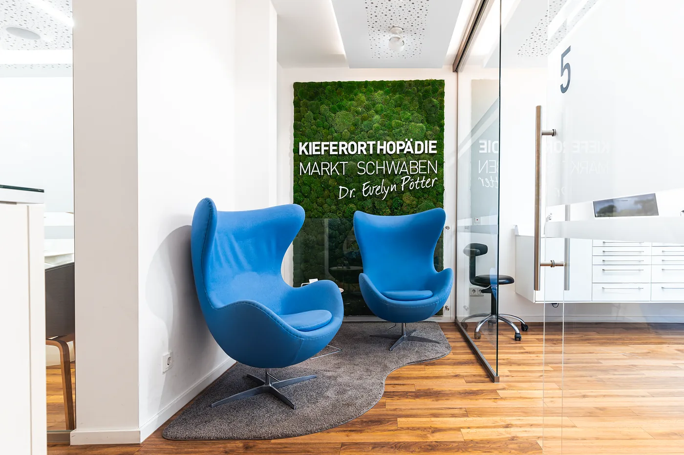 Lounge mit blauen Sesseln vor der Mooswand der Praxis